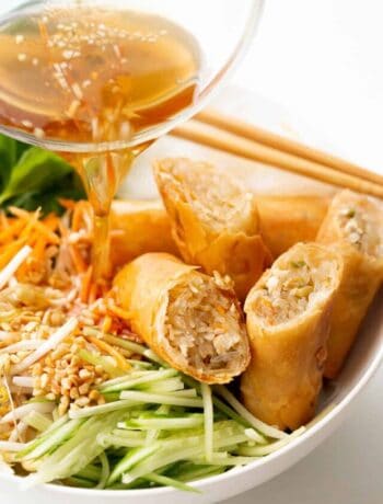 Pouring nuoc mam sauce over a Vietnamese noodle bowl topped with spring rolls.