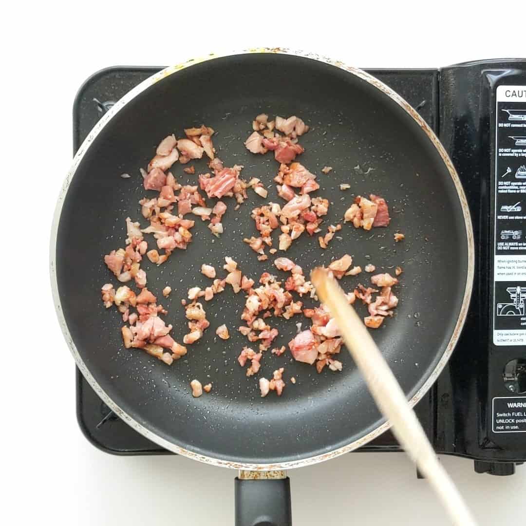 Bacon pieces cooking in a frying pan.