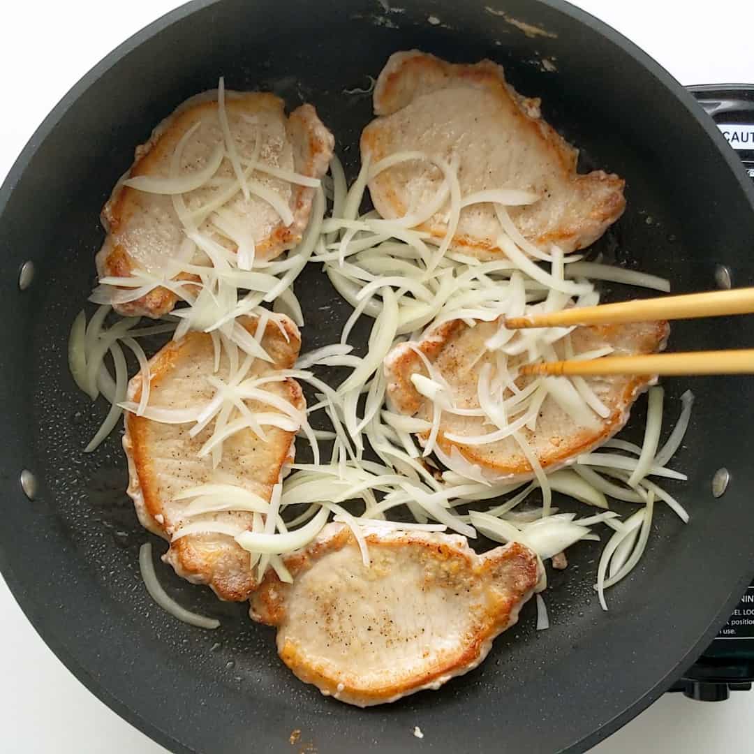 Frying pork steaks with thinly sliced onion.
