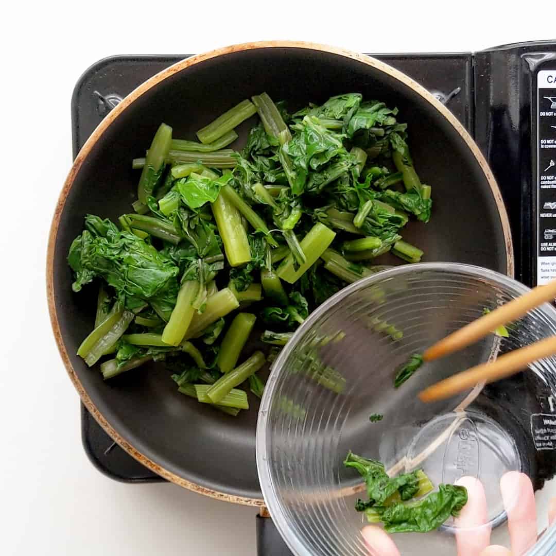 Placing blanched spinach in a frying pan.