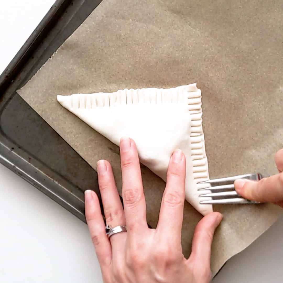 Pressing the edges of the puff pastry with a fork to seal.