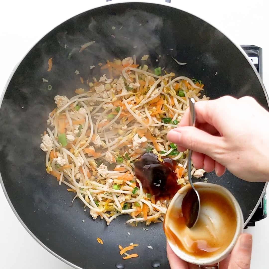 Pouring oyster sauce into wok with the fried chicken and vegetables.