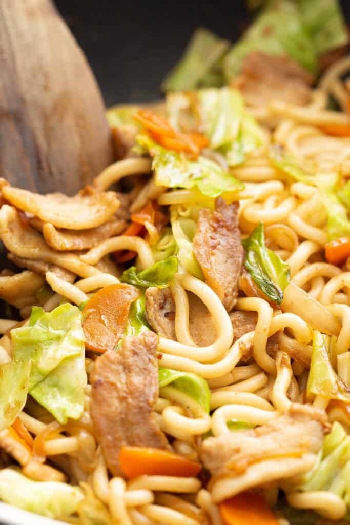 Yaki udon in a wok with wooden spatula.