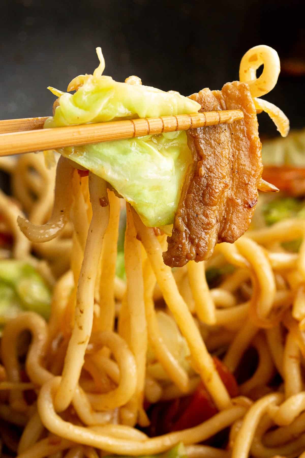 Pork, cabbage and udon noodles on a chopstick.