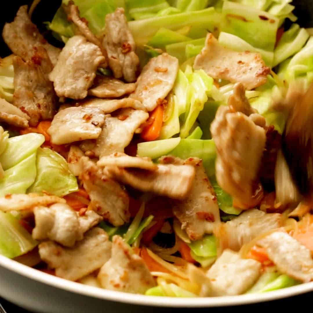Stir frying the pork and vegetables in a wok.
