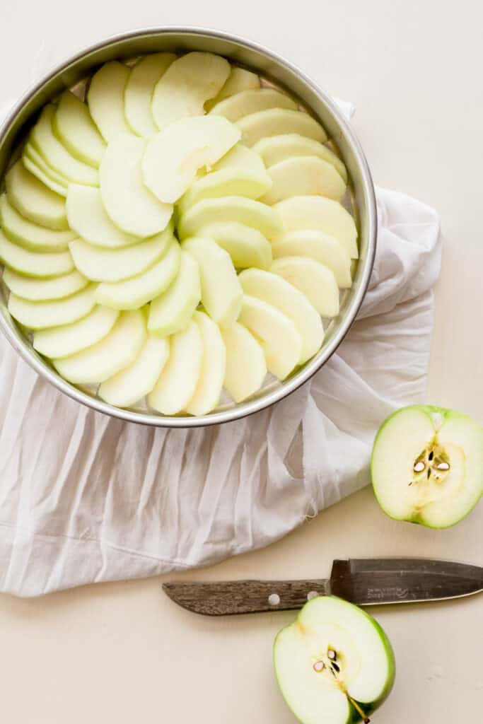 Apple slices arranged decoratively in a round baking dish, with another sliced apple and knife next to it.