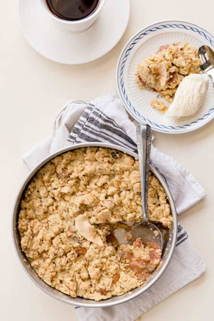 Top down view of the freshly baked apple crumble with a portion served out on a plate with ice cream.