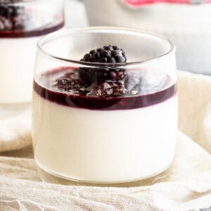 A glass filled with blancmange pudding and topped with blackberry coulis.