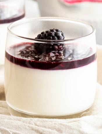 A glass filled with blancmange pudding and topped with blackberry coulis.