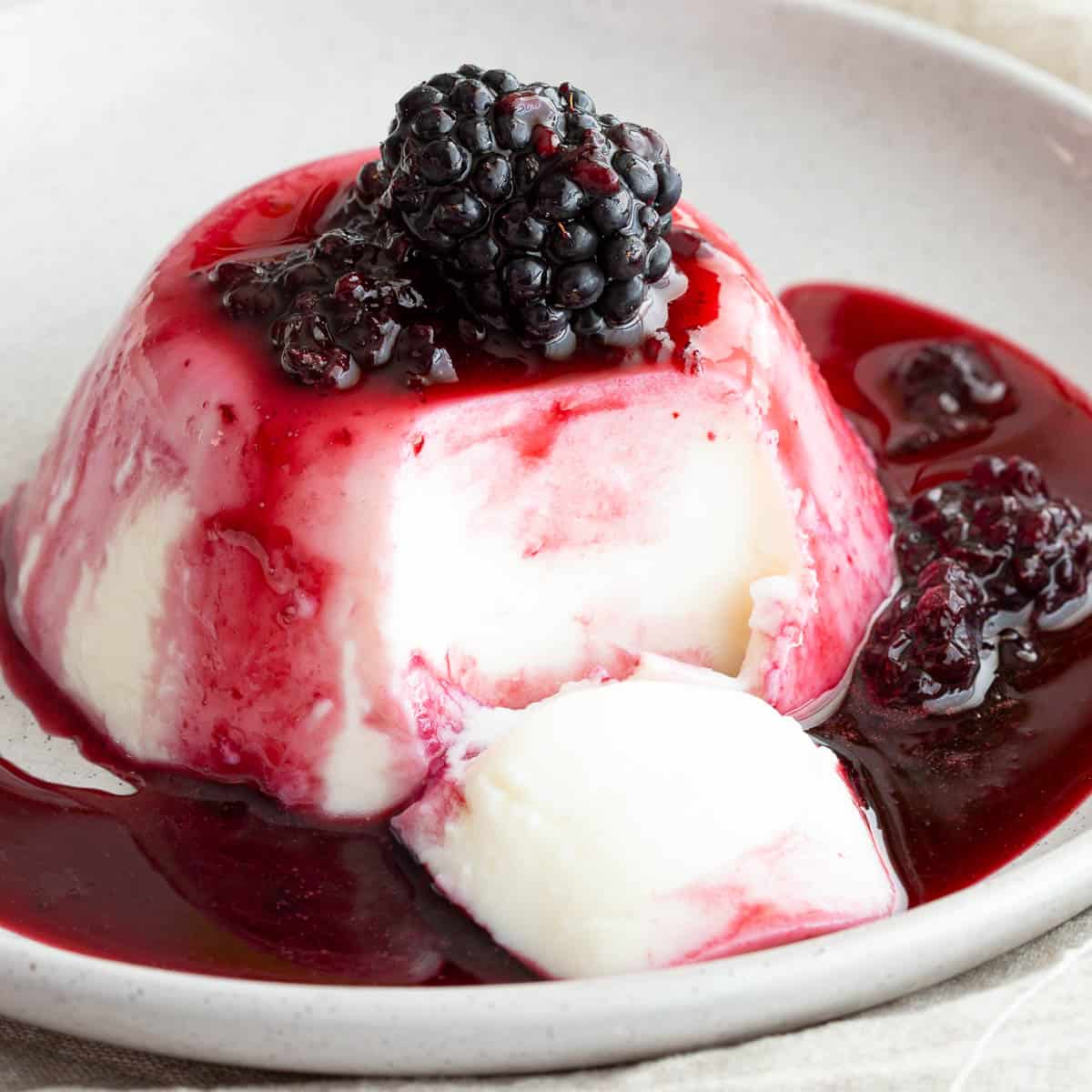 Close up shot of set blancmange with blackberry coulis and an extra berry on top.