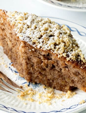 A brown, diamond shaped Greek cake topped with nuts and icing sugar.