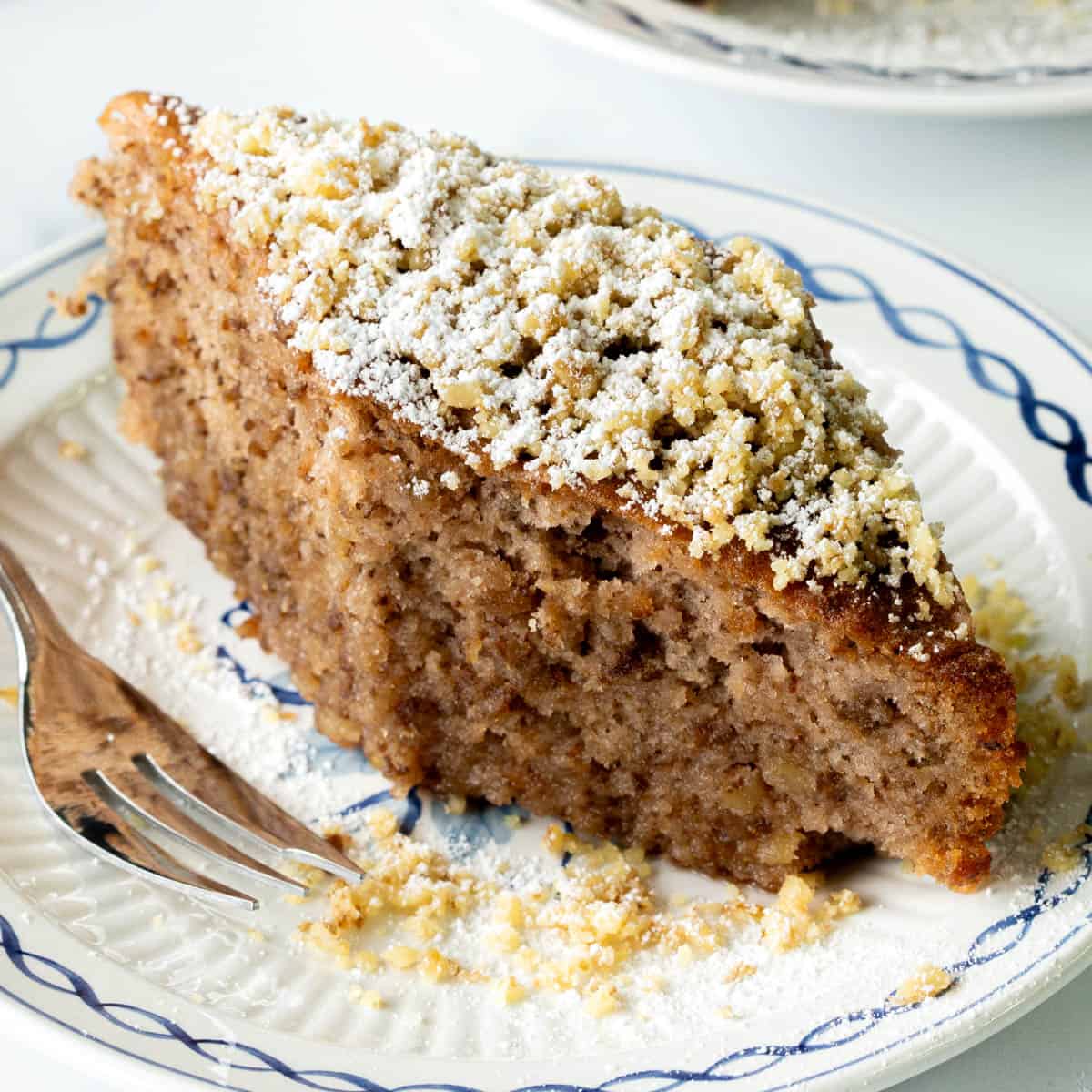 A brown, diamond shaped Greek cake topped with nuts and icing sugar.