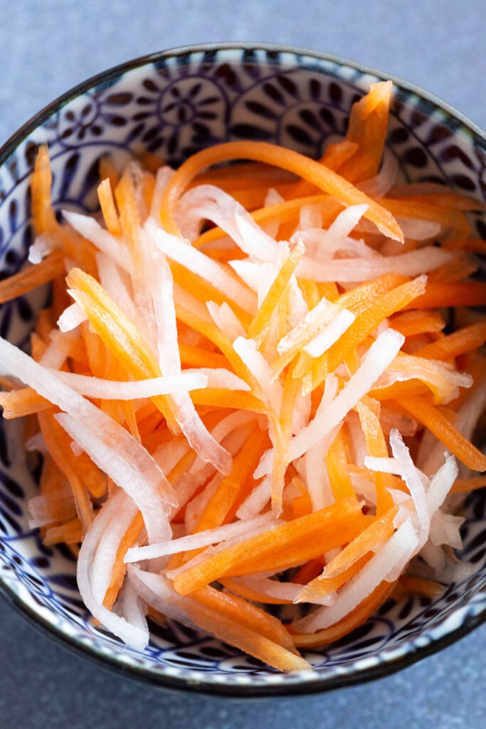 Strips of quick pickled carrots and daikon in a small dish.