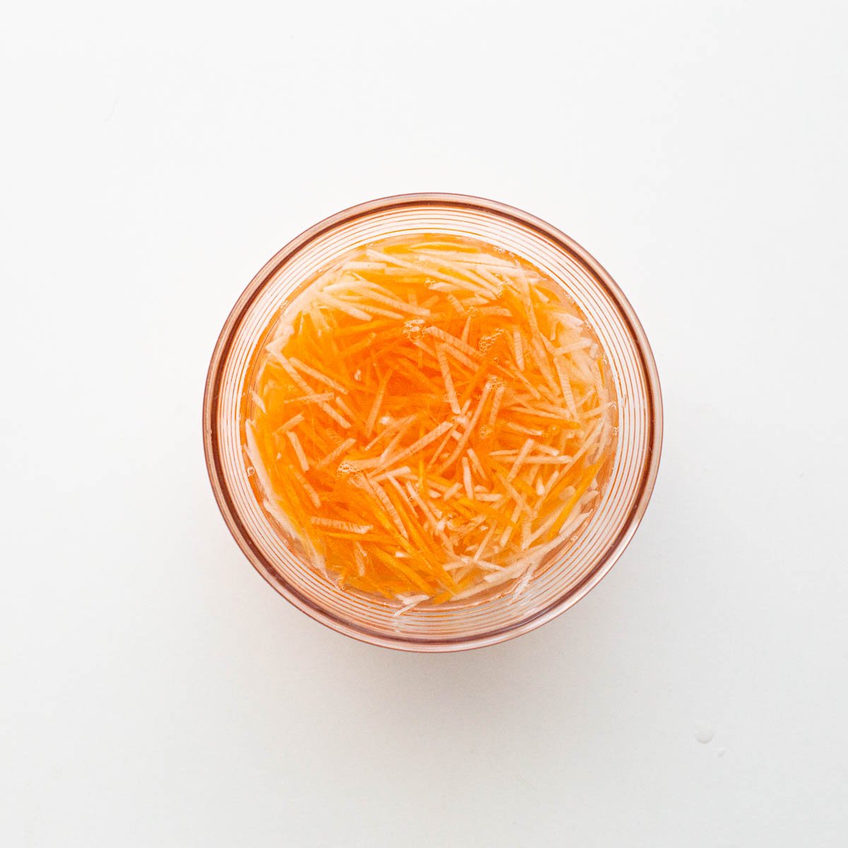 Soaking carrot and daikon in salt solution in a glass bowl.