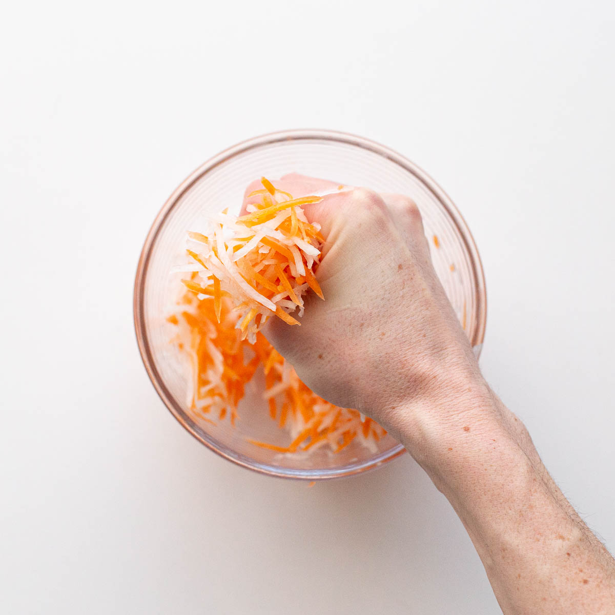 A hand squeezing out excess water from the carrot and daikon.