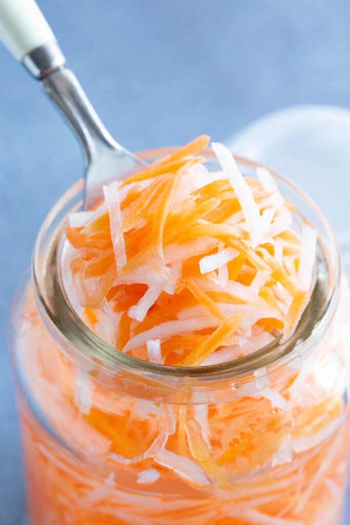 A large scoop of pickled carrots and daikon on a fork.