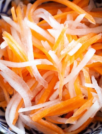Strips of quick pickled carrots and daikon in a small dish.