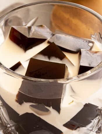 A glass filled with coffee jelly cubes and fresh cream poured over it.