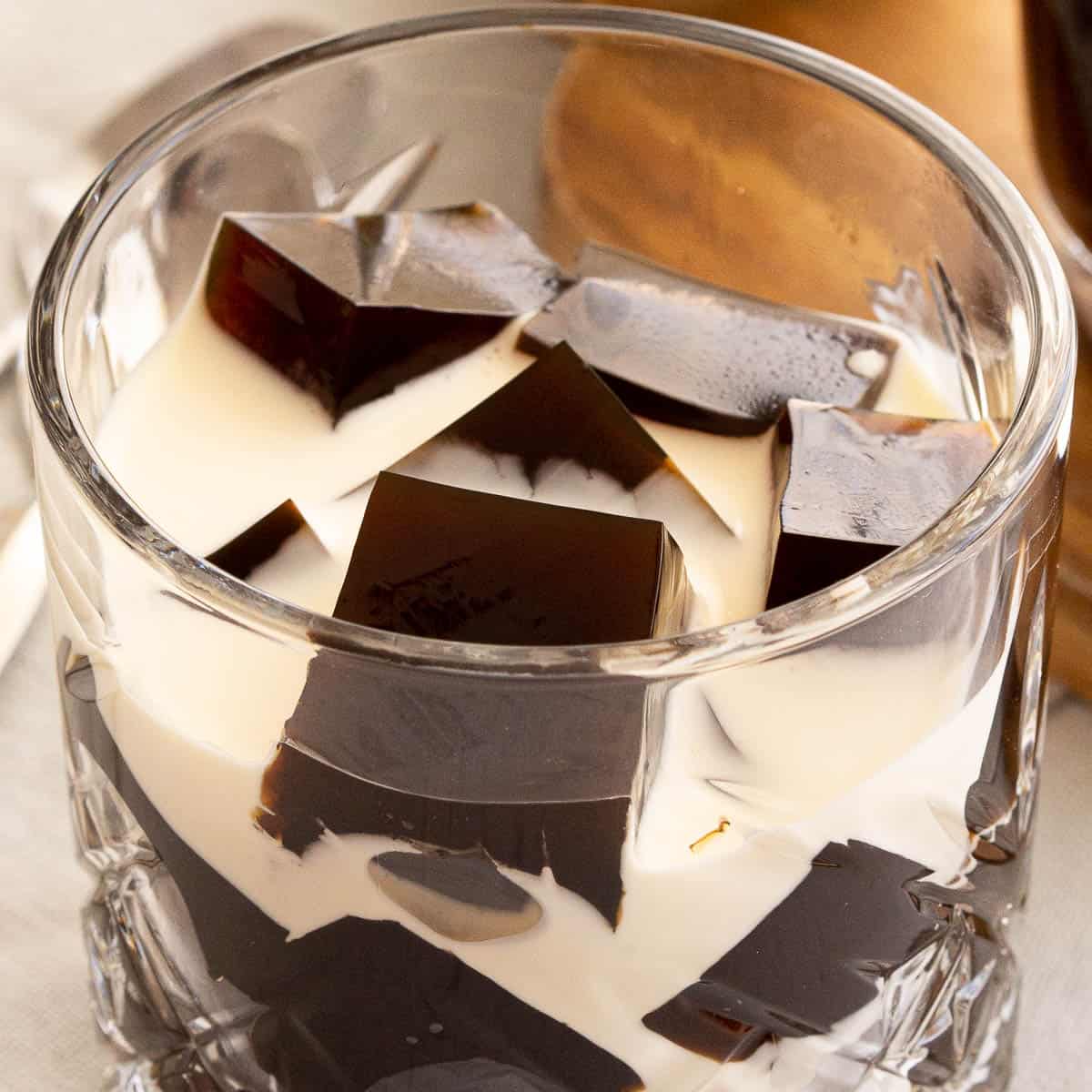 A glass filled with coffee jelly cubes and fresh cream poured over it.