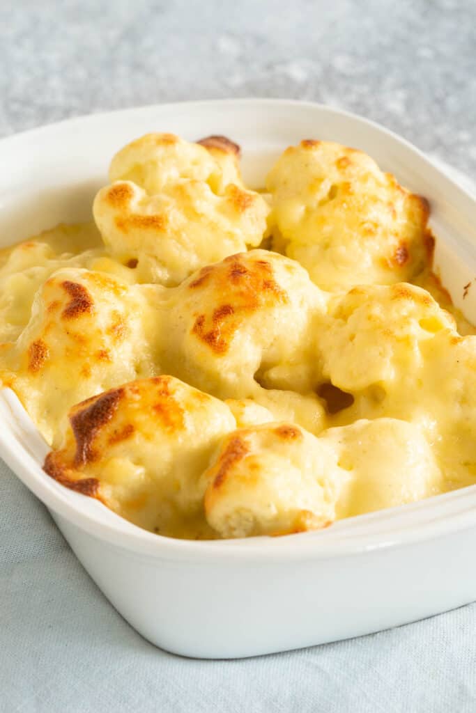 A large dish of cauliflower florets, topped with a creamy cheesy white sauce.