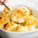 A hand peeks out of the corner as it scoops up a large spoonful of cauliflower cheese.