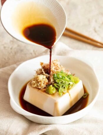 A hand is pouring a small dish of soy sauce over the Japanese cold tofu.