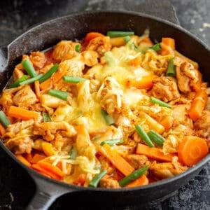Dakgalbi in a black cast iron skillet with melted cheese on top, ready to eat.