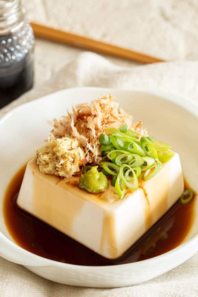 Square piece of silken tofu in a shallow white dish with soy sauce.