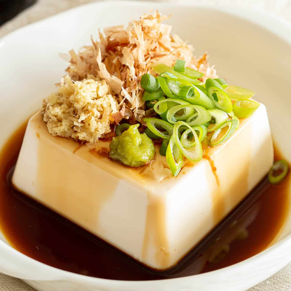 Hiyayakko in a white dish in a shallow pool of soy sauce.