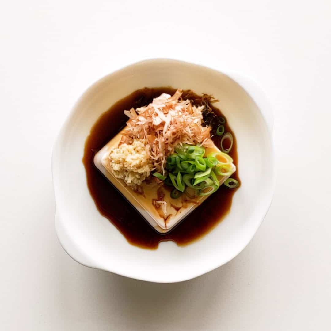 A square of silken tofu topped with spring onion, ginger, wasabi and bonito flakes.