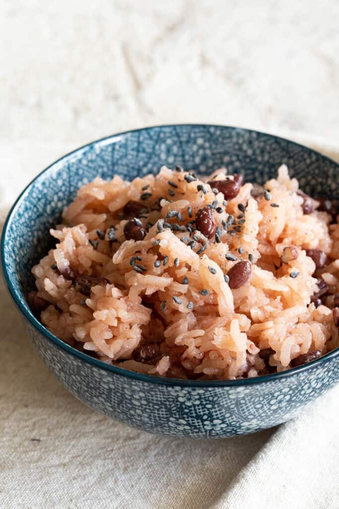 Pink sticky rice and red beans garnished with black sesame seeds in a blue bowl.