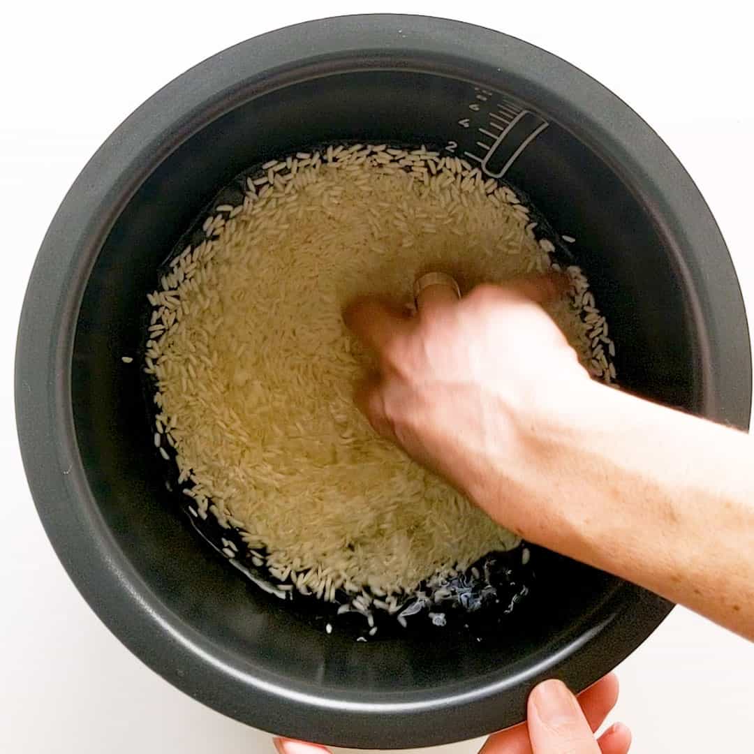 Rinsing sticky rice in a black rice cooker bowl.