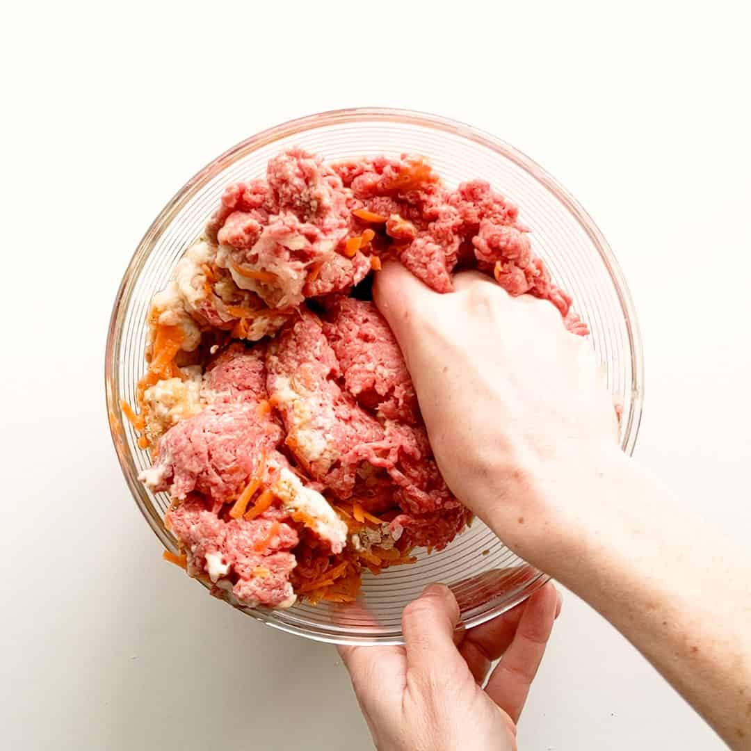 Mixing rissole mixture with hands.