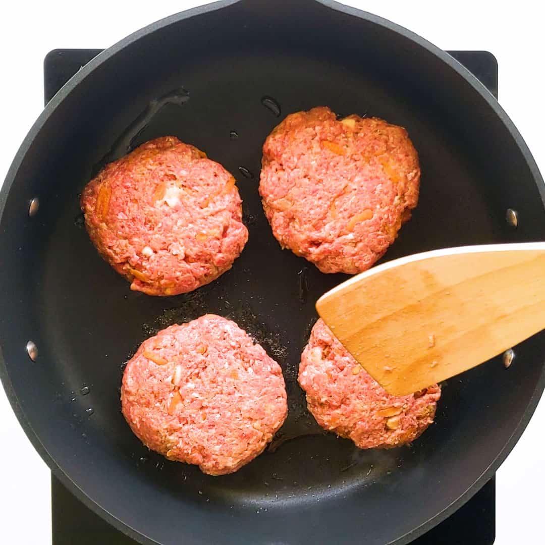 Four beef rissoles cooking in a pan.