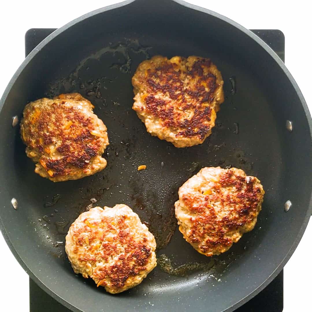 Four cooked beef rissoles sitting in a pan, ready to be served.