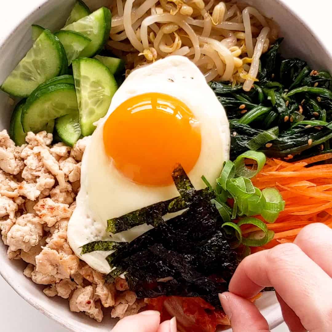 Strips of seasoned seaweed are placed on top of a bibimbap rice bowl for the final touch.