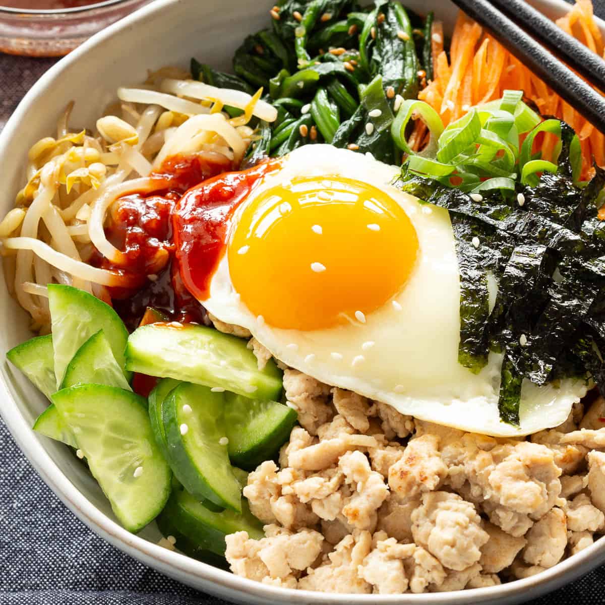 A sunny side-up egg glows on top of a bowl of Chicken Bibimbap.