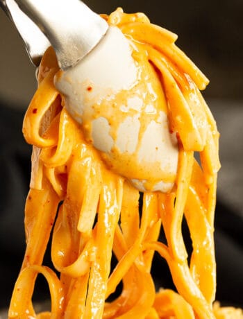 A pair of tongs holds up super creamy gochujang pasta, ready to plate.