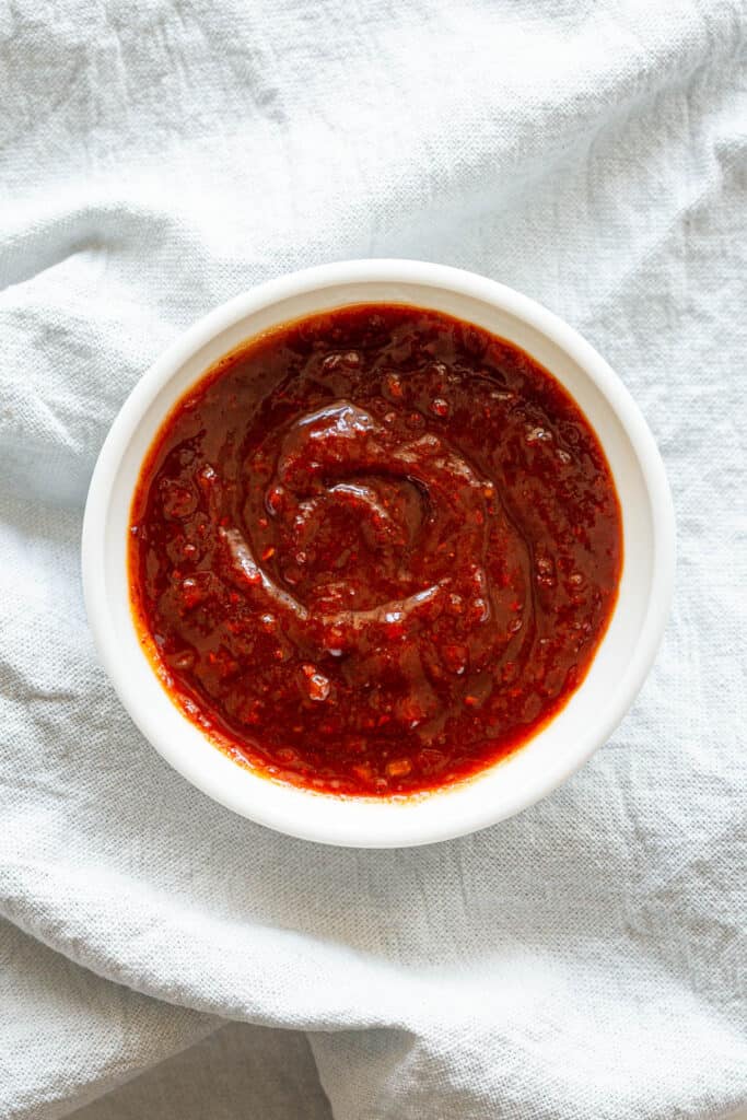 A top down view of a homemade gochujang sauce in a small dish, which sits on a tea towel.