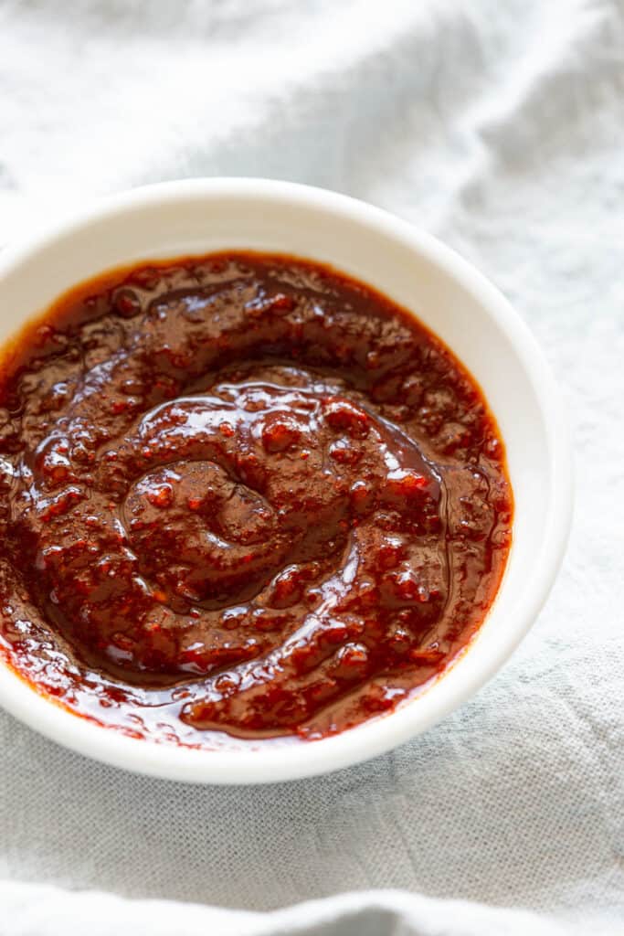 A dark red sauce with swirls sits in a small white dish.