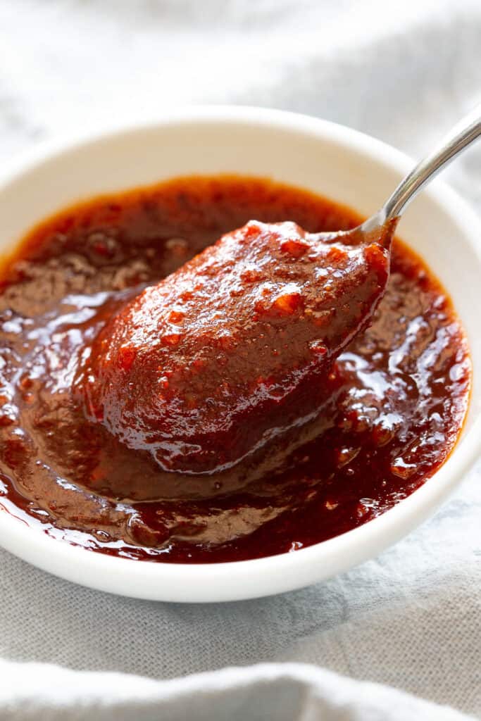 A spoon scoops up some red gochujang sauce in a little white dish.