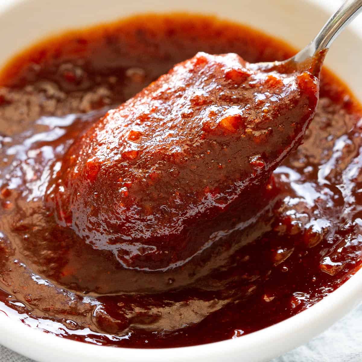 A spoon scoops out some all purpose gochujang sauce from a small white dish.