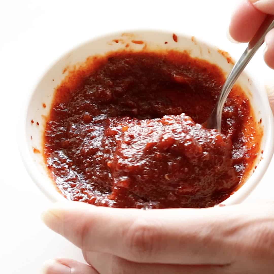 A hand is mixing the gochujang sauce together with a spoon.