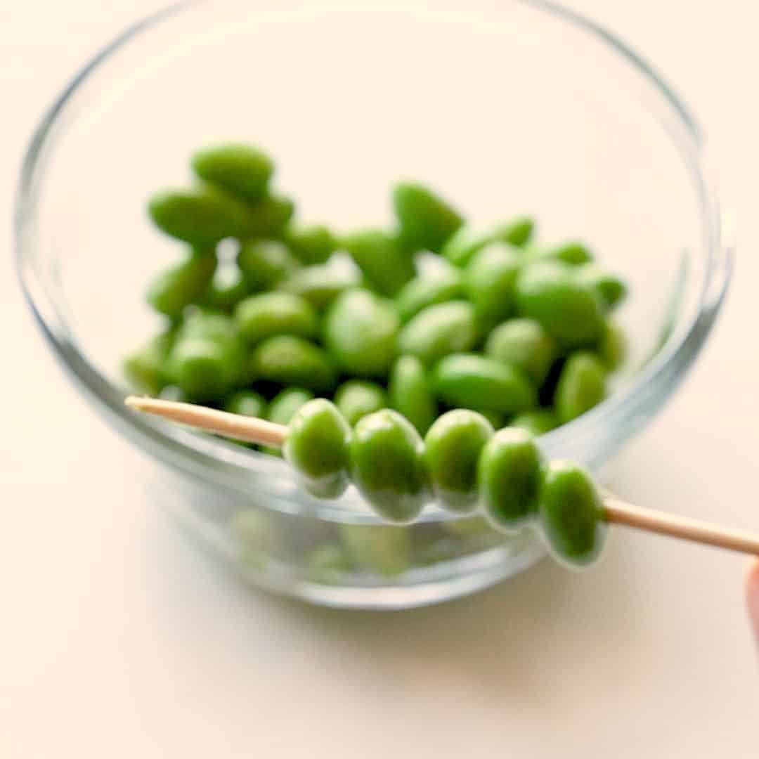 Putting edamame beans onto a skewer.