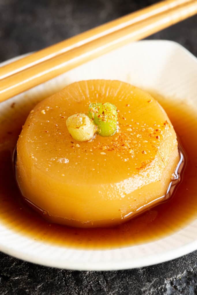 A golden piece of Japanese simmered daikon sits in a shallow white dish.