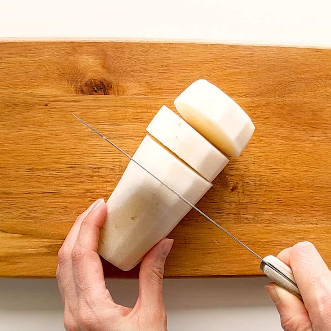 Slicing a long peeled daikon into thick round pieces.