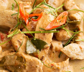 Thinly sliced lime leaves and chilli are topped on a bowl of Panang chicken curry.