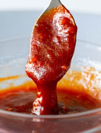 A spoon dips into a bowl of bibimbap sauce.