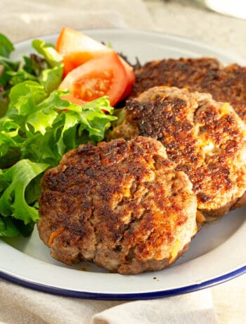 Three beef rissoles on a plate with lettuce and tomato.