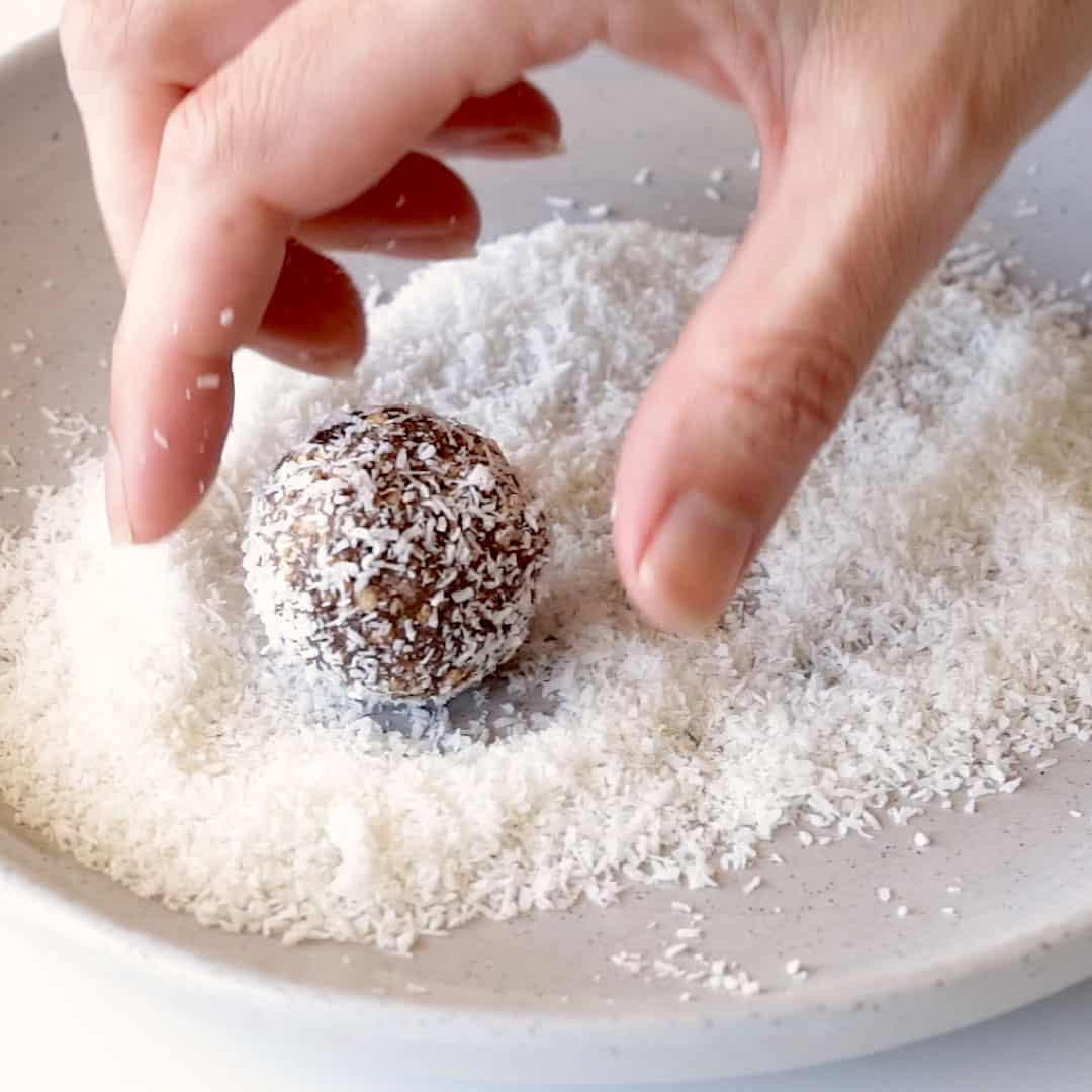 A hand is about to pick up a choc coconut ball coated in desiccated coconut.